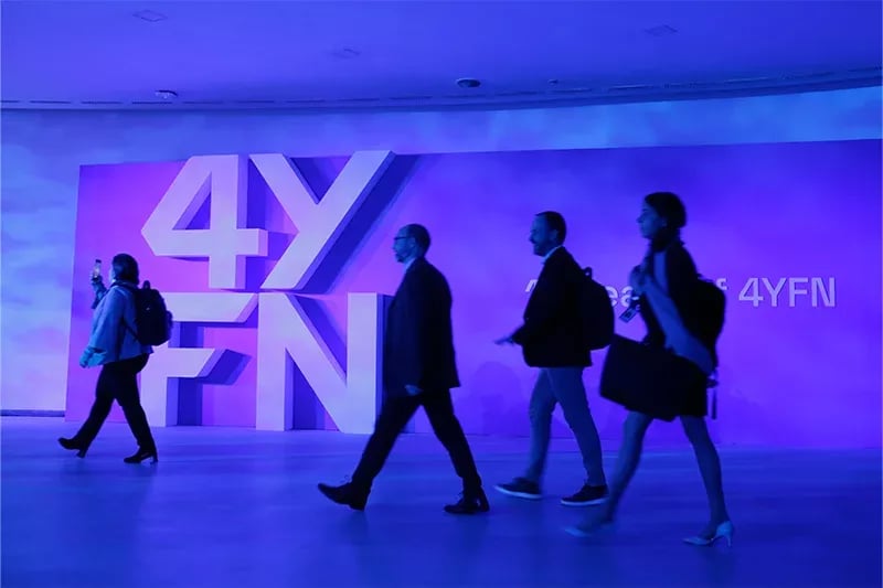 Attendees walking past a large illuminated '4YFN' sign in a vibrant purple-lit hallway at a conference or exhibition.
