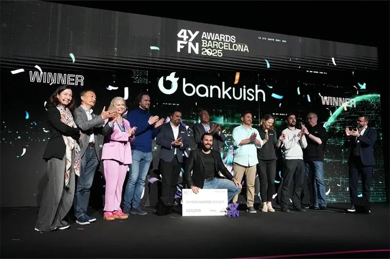 Award ceremony at 4YFN 2025, celebrating Bankuish as the winner. A group of people stands on stage, clapping and smiling, while a representative of Bankuish kneels in the front holding a large check for €20,000. The backdrop displays '4YFN Awards Barcelona 2025' and 'Bankuish Winner,' with confetti falling to mark the occasion.