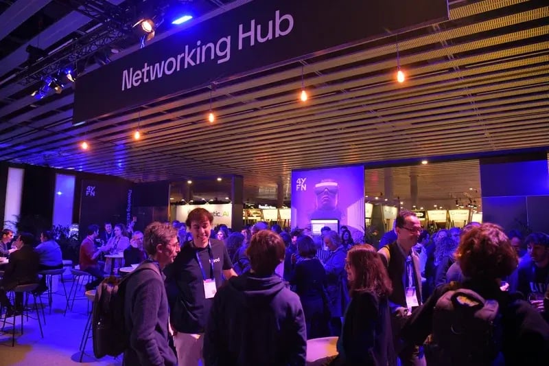 A bustling networking event with people engaging in conversations under a sign reading "Networking Hub." The atmosphere is lively and collaborative.