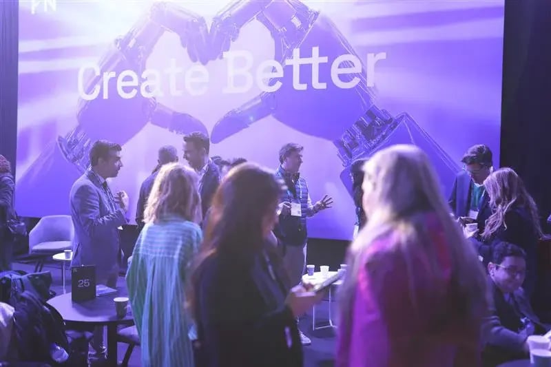 The image depicts a networking area at the 4YFN (4 Years From Now) event, with attendees gathered in a vibrant and energetic space. The background features a large digital display with the phrase "Create Better," accompanied by a futuristic visual of robotic hands shaking, symbolizing collaboration and innovation. People are conversing and engaging in discussions, with some holding cups and looking at their phones. The atmosphere is professional yet relaxed, focused on creating new opportunities and fostering connections among attendees.