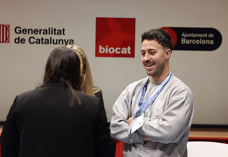 Smiling man wearing a conference badge and lanyard engages in conversation with two women at the 4YFN event, with logos of Generalitat de Catalunya, Biocat, and Ajuntament de Barcelona visible in the background.